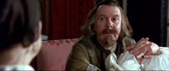 Movie still from “Girl with a Pearl Earring” (2003), directed by Peter Webber – A man sitting on top of a couch wearing a wig; Close Up shot, Over the shoulder angle