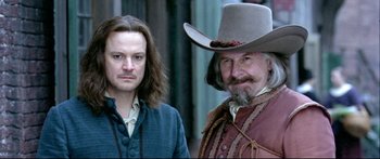 Movie still from “Girl with a Pearl Earring” (2003), directed by Peter Webber – A man in a cowboy hat and a man with long hair; Close Up shot, Over the shoulder angle