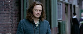 Movie still from “Girl with a Pearl Earring” (2003), directed by Peter Webber – A man with long brown hair standing in front of a building; Close Up shot, Over the shoulder angle