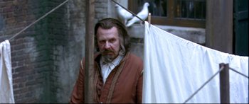 Movie still from “Girl with a Pearl Earring” (2003), directed by Peter Webber – A man with long hair and a beard standing next to a white flag; Medium shot, Over the shoulder angle