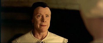 Movie still from “Girl with a Pearl Earring” (2003), directed by Peter Webber – An older woman wearing a black hat and a white shirt; Close Up shot, Low angle