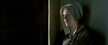 Movie still from “Girl with a Pearl Earring” (2003), directed by Peter Webber – A young woman wearing a hood in a room; Close Up shot, Low angle
