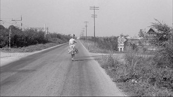 Movie still from “Girl with a Suitcase” (1961), directed by Valerio Zurlini – An older woman riding a bicycle down a road; Wide shot, High angle