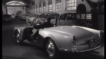 Movie still from “Girl with a Suitcase” (1961), directed by Valerio Zurlini – An old fashioned car is parked in a garage; Wide shot, High angle