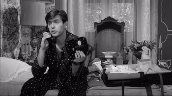 Movie still from “Girl with a Suitcase” (1961), directed by Valerio Zurlini – A man holding a camera while sitting on a bed; Medium shot, High angle