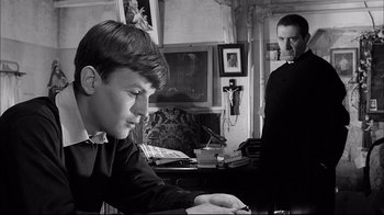 Movie still from “Girl with a Suitcase” (1961), directed by Valerio Zurlini – A young man sitting at a desk in front of another man in a room; Medium shot, Over the shoulder angle