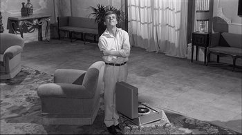 Movie still from “Girl with a Suitcase” (1961), directed by Valerio Zurlini – A man standing in a living room with his arms crossed; Wide shot, High angle