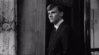 Movie still from “Girl with a Suitcase” (1961), directed by Valerio Zurlini – A man in a suit and tie standing in front of a wooden door; Close Up shot, Low angle