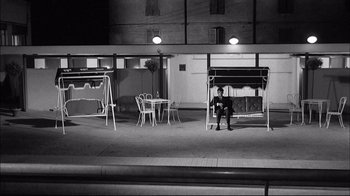Movie still from “Girl with a Suitcase” (1961), directed by Valerio Zurlini – A man sitting on top of a bench next to a table; Wide shot, High angle