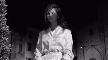 Movie still from “Girl with a Suitcase” (1961), directed by Valerio Zurlini – A woman in a white shirt is standing in a black and white photo; Medium shot, Low angle