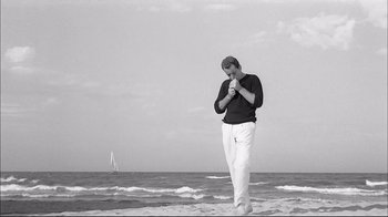Movie still from “Girl with a Suitcase” (1961), directed by Valerio Zurlini – A man standing on a beach near the ocean; Wide shot, Low angle