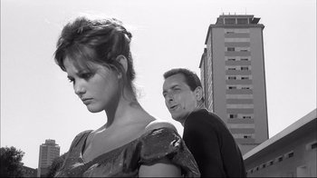 Movie still from “Girl with a Suitcase” (1961), directed by Valerio Zurlini – A man and a woman standing next to each other in front of a tall building; Medium shot, Low angle