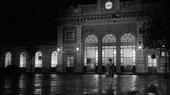 Movie still from “Girl with a Suitcase” (1961), directed by Valerio Zurlini – A woman is standing in front of a large building at night; Extreme Wide shot, Low angle