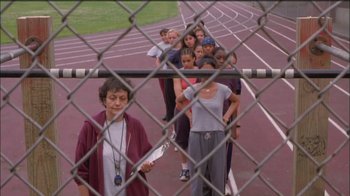 Movie still from “Girlfight” (2000), directed by Karyn Kusama – A group of people standing behind a chain link fence on top of a track; Medium shot, High angle