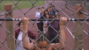 Movie still from “Girlfight” (2000), directed by Karyn Kusama – A group of people standing behind a chain link fence; Wide shot, High angle