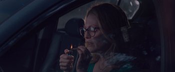 Movie still from “Gloria Bell” (2018), directed by Sebastián Lelio – A woman smoking a cigarette while sitting in a car; Medium shot, High angle