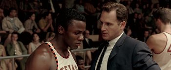 Movie still from “Glory Road” (2006), directed by James Gartner – A man and a man in a suit talking to each other in front of an audience; Close Up shot, Over the shoulder angle