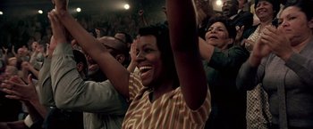 Movie still from “Glory Road” (2006), directed by James Gartner – A group of people in a room raising their hands; Medium shot, High angle