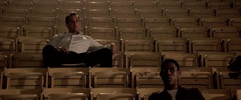 Movie still from “Glory Road” (2006), directed by James Gartner – A man sitting in an empty auditorium with another man standing in the background; Wide shot, Low angle