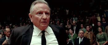 Movie still from “Glory Road” (2006), directed by James Gartner – An older man wearing a suit and tie in front of an audience; Close Up shot, Low angle