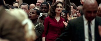 Movie still from “Glory Road” (2006), directed by James Gartner – A woman in a red dress standing in front of a group of people; Medium shot, Over the shoulder angle