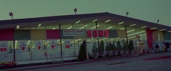 Movie still from “Go” (1999), directed by Doug Liman – A store front with a lot of signs on the windows; Extreme Wide shot, Low angle