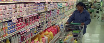 Movie still from “Go” (1999), directed by Doug Liman – A person in a shopping cart next to a shelf filled with lots of milk and juice; Medium shot, High angle