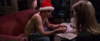 Movie still from “Go” (1999), directed by Doug Liman – A shirtless man wearing a santa clause hat and sitting at a dinner table; Medium shot, Low angle