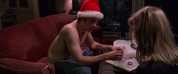 Movie still from “Go” (1999), directed by Doug Liman – A man sitting at a table wearing a santa hat; Medium shot, Low angle