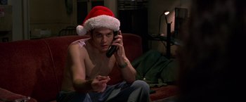 Movie still from “Go” (1999), directed by Doug Liman – A man sitting on a couch talking on a cell phone wearing a santa hat; Medium shot, Low angle