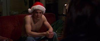 Movie still from “Go” (1999), directed by Doug Liman – A man sitting on a couch wearing a santa hat; Medium shot, Low angle