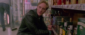 Movie still from “Go” (1999), directed by Doug Liman – A man in a leather jacket leaning on a shelf; Close Up shot, Over the shoulder angle