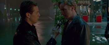 Movie still from “Go” (1999), directed by Doug Liman – A man holding a cell phone in his hand while another man holds a cell phone; Close Up shot, Over the shoulder angle