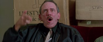 Movie still from “Go” (1999), directed by Doug Liman – An older man in a black shirt and a tie; Close Up shot, Low angle