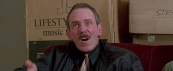 Movie still from “Go” (1999), directed by Doug Liman – An older man wearing a black shirt and a tie; Close Up shot, Low angle