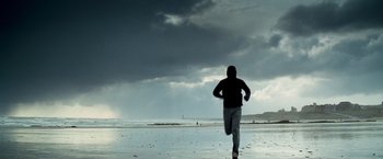 Movie still from “Goal! The Dream Begins” (2005), directed by Michael Winterbottom – A man running on the beach under a cloudy sky; Wide shot, Low angle