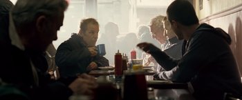 Movie still from “Goal! The Dream Begins” (2005), directed by Michael Winterbottom – A group of people sitting at a table with drinks and condiments; Medium shot, Over the shoulder angle