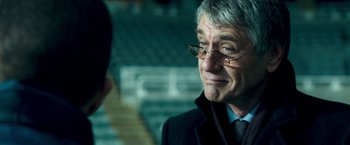 Movie still from “Goal! The Dream Begins” (2005), directed by Michael Winterbottom – An older man wearing glasses and a jacket; Close Up shot, Over the shoulder angle