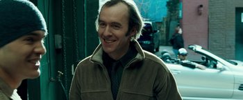 Movie still from “Goal! The Dream Begins” (2005), directed by Michael Winterbottom – A man smiling while standing on the side of the street; Close Up shot, Over the shoulder angle