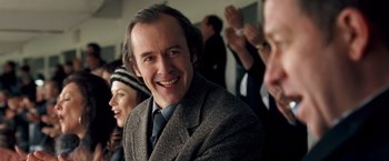 Movie still from “Goal! The Dream Begins” (2005), directed by Michael Winterbottom – A man in a suit and tie smiling for the camera; Close Up shot, Over the shoulder angle