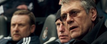 Movie still from “Goal! The Dream Begins” (2005), directed by Michael Winterbottom – A man with glasses is sitting next to another man; Close Up shot, Over the shoulder angle