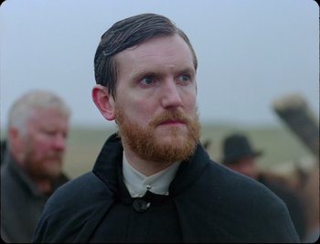 A man with a long beard and a mustache wearing a black coat