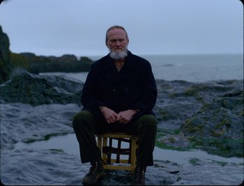 An older man sitting on a chair on the beach