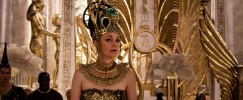 Movie still from “Gods of Egypt” (2016), directed by Alex Proyas – A woman in a gold and black dress wearing a crown; Close Up shot, Over the shoulder angle