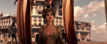 Movie still from “Gods of Egypt” (2016), directed by Alex Proyas – A beautiful woman wearing a crown sitting in a chair; Medium shot, Low angle