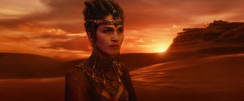 Movie still from “Gods of Egypt” (2016), directed by Alex Proyas – A woman in a dress and a headpiece in front of a sunset; Close Up shot, Over the shoulder angle