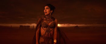 Movie still from “Gods of Egypt” (2016), directed by Alex Proyas – A beautiful woman in a costume standing in front of a sunset; Medium shot, High angle
