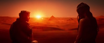 Movie still from “Gods of Egypt” (2016), directed by Alex Proyas – A person sitting on the ground in front of the pyramids; Extreme Wide shot, High angle