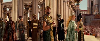 Movie still from “Gods of Egypt” (2016), directed by Alex Proyas – A group of people in costumes standing in front of a building; Medium shot, Over the shoulder angle