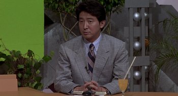 Movie still from “Godzilla vs. Destoroyah” (1995), directed by Ishirô Honda – A man sitting at a table in front of a plant; Medium shot, Over the shoulder angle